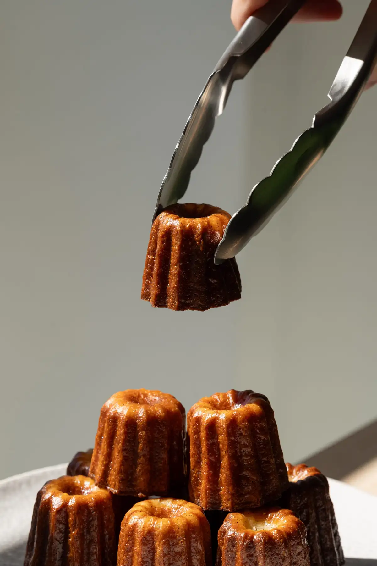 Cannelé bordelais au rhum Moon Harbour saisi à la pince au-dessus d'une assiette, Quatre-Quarts Bordeaux