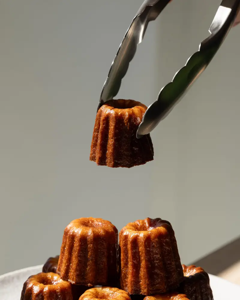 Cannelé bordelais au rhum Moon Harbour saisi à la pince au-dessus d'une assiette, Quatre-Quarts Bordeaux