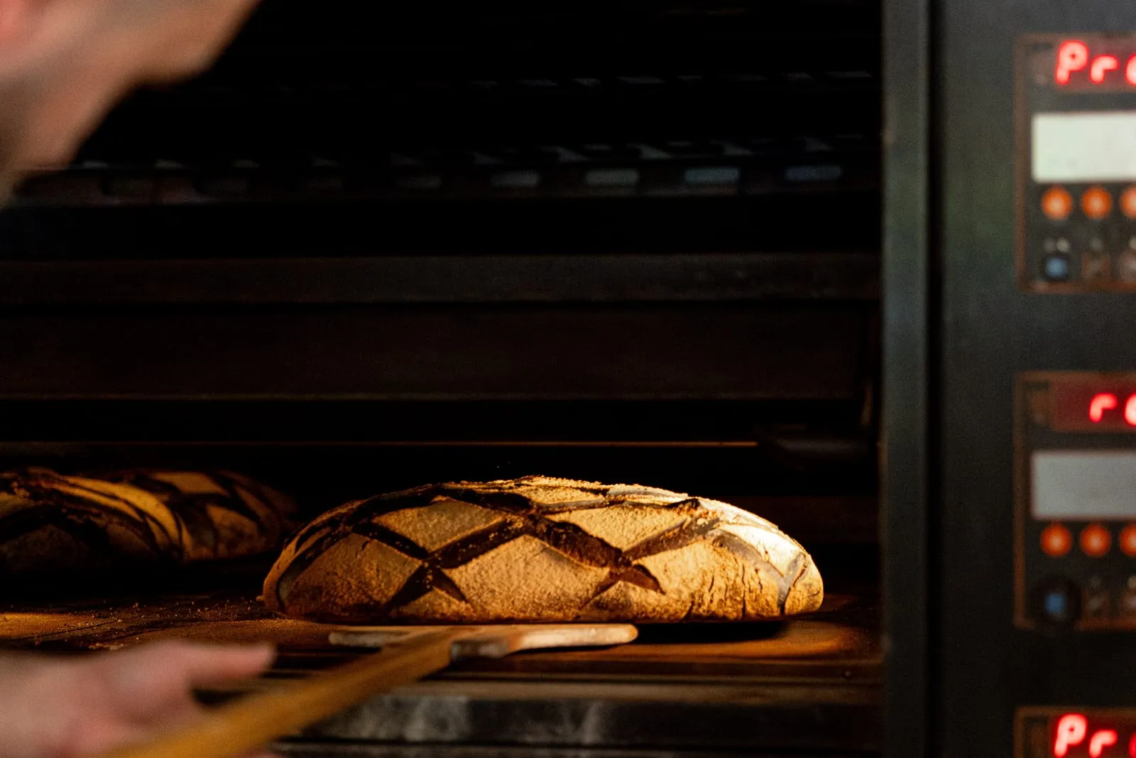 Boulanger enfournant un pain au levain à la pelle dans le four, boulangerie Qu4tre-Qu4rts