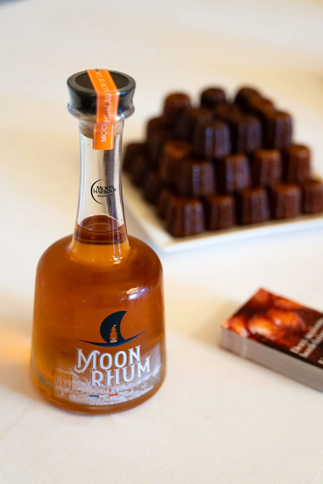 Bouteille de Moon Rhum de la distillerie Moon Harbour devant une pyramide de cannelés Qu4tre-Qu4rts